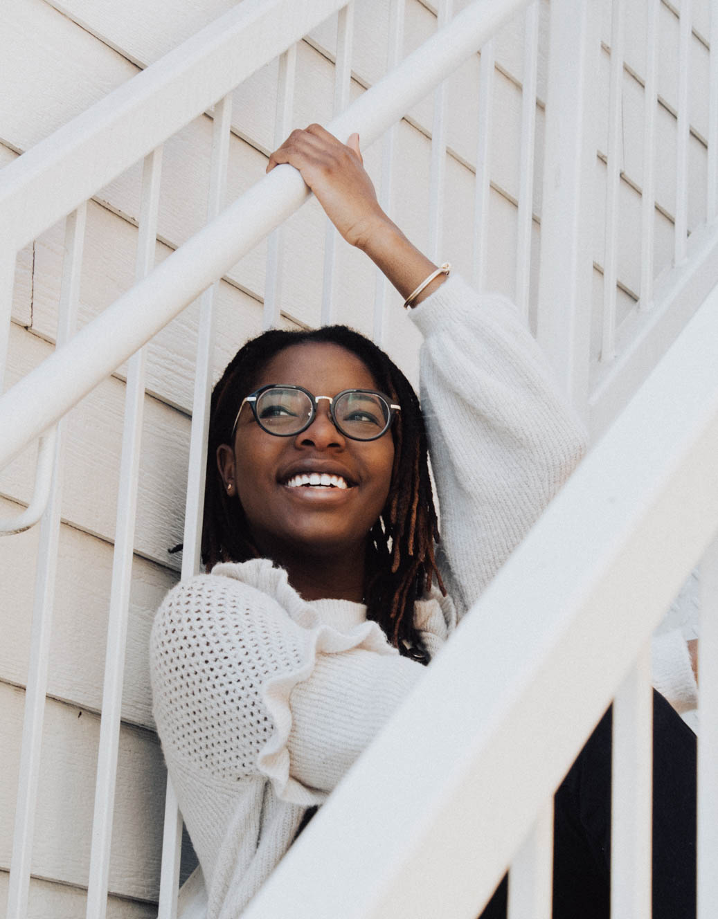 A smiling woman in a white sweater standing beside a white staircase